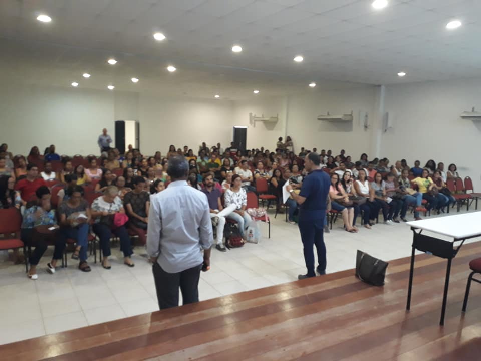 palestrantes falam ao microfone para plateia de dezenas de pessoas sentadas