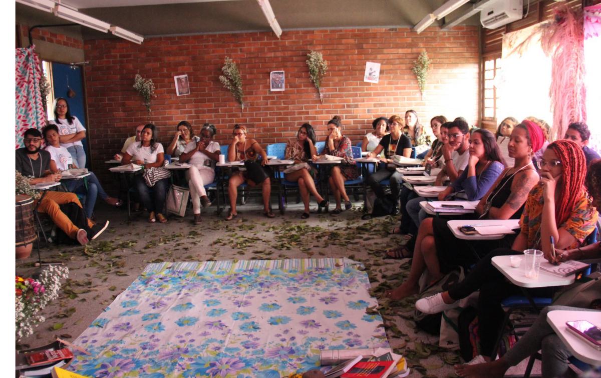 Participantes reunidos em círculo, sentados em cadeiras, folhas secas ao chão no centro do círculo