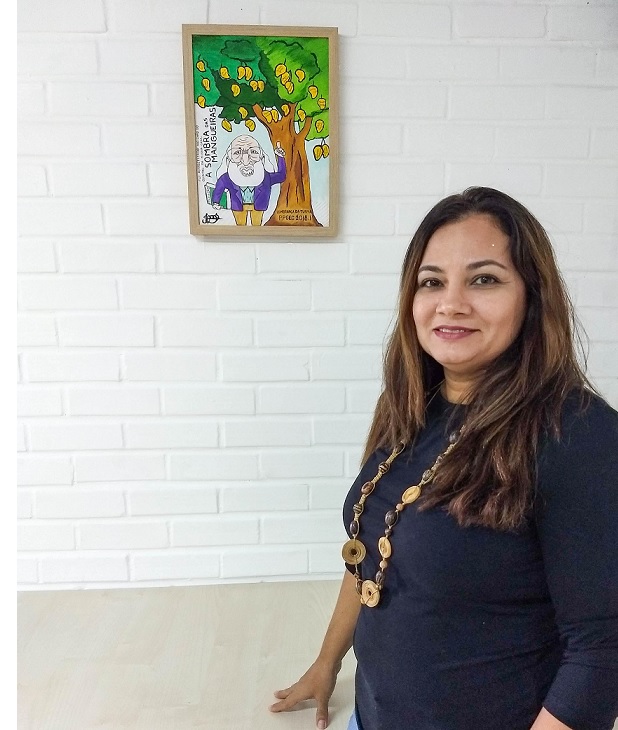 Professora Mônica Folena ao lado de quadro de Paulo Freire