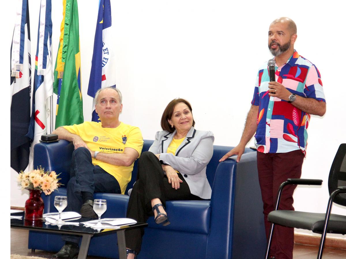 professor hugo monteiro ao microfone, de pé, enquanto a reitora e o vice-reitor assistem à palestra sentados num sofá