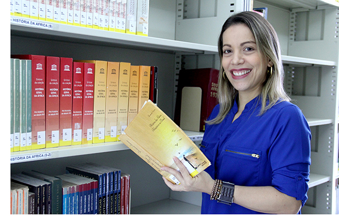 servidora da ufrpe segurando livro. ao fundo, prateleira com livros