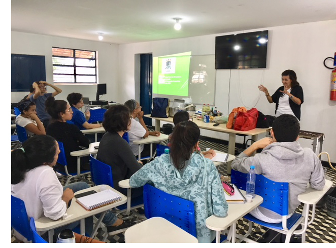 Participantes da aula prática sentados em sala de aula, enquanto professora explica conteúdos