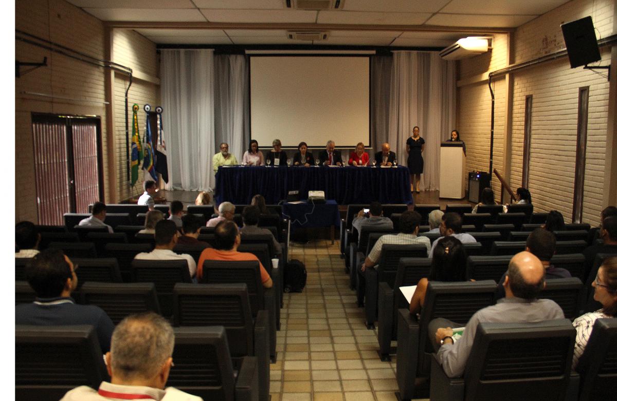 foto do auditório da Pró-reitoria de extensao. Pessoas sentadas nas poltronas, foto tirada dos fundos, voltada para o palco principal do auditório