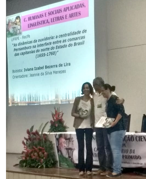 premiação sendo entregue à estudante da UFRPE, no palco do auditório da Facepe